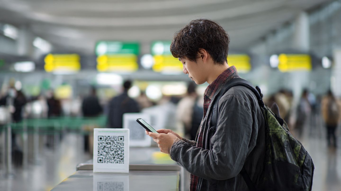 Traveler scanning QR code to activate eSIM at Tokyo Haneda Airport before attending the Japan Mobility Show — tech-focused travel moment, instructional purpose
