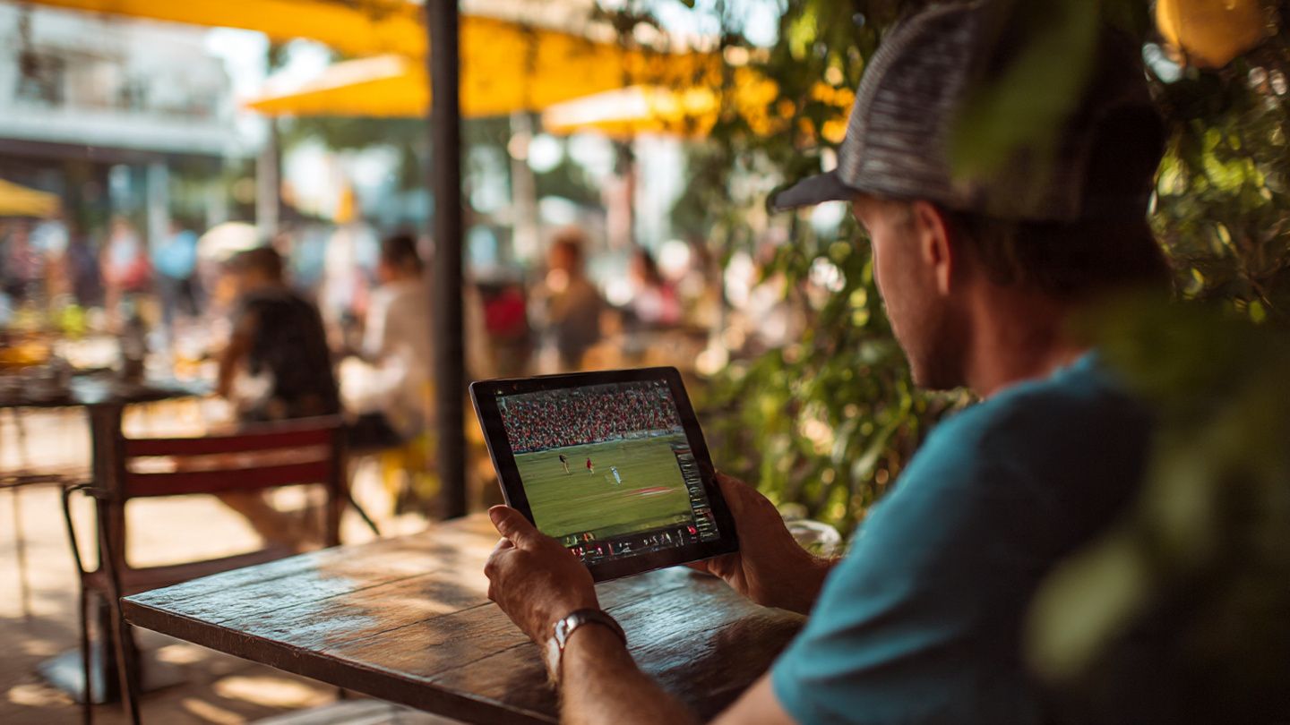 Traveler sitting at a café abroad watching a cricket match on a tablet, showing easy international streaming with eSIM connectivity