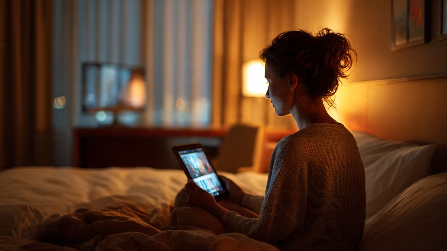 Traveler sitting in a hotel room watching BBC World News on a tablet using Yoho eSIM connection, warm ambient lighting, relaxed atmosphere