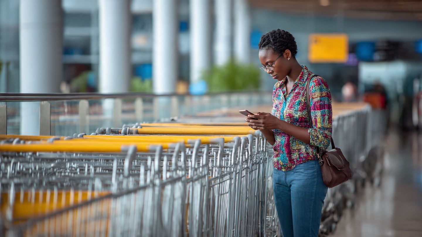 Traveler using a smartphone at Bamako airport with luggage carts in the background; clean, editorial travel-tech style focusing on eSIM activation