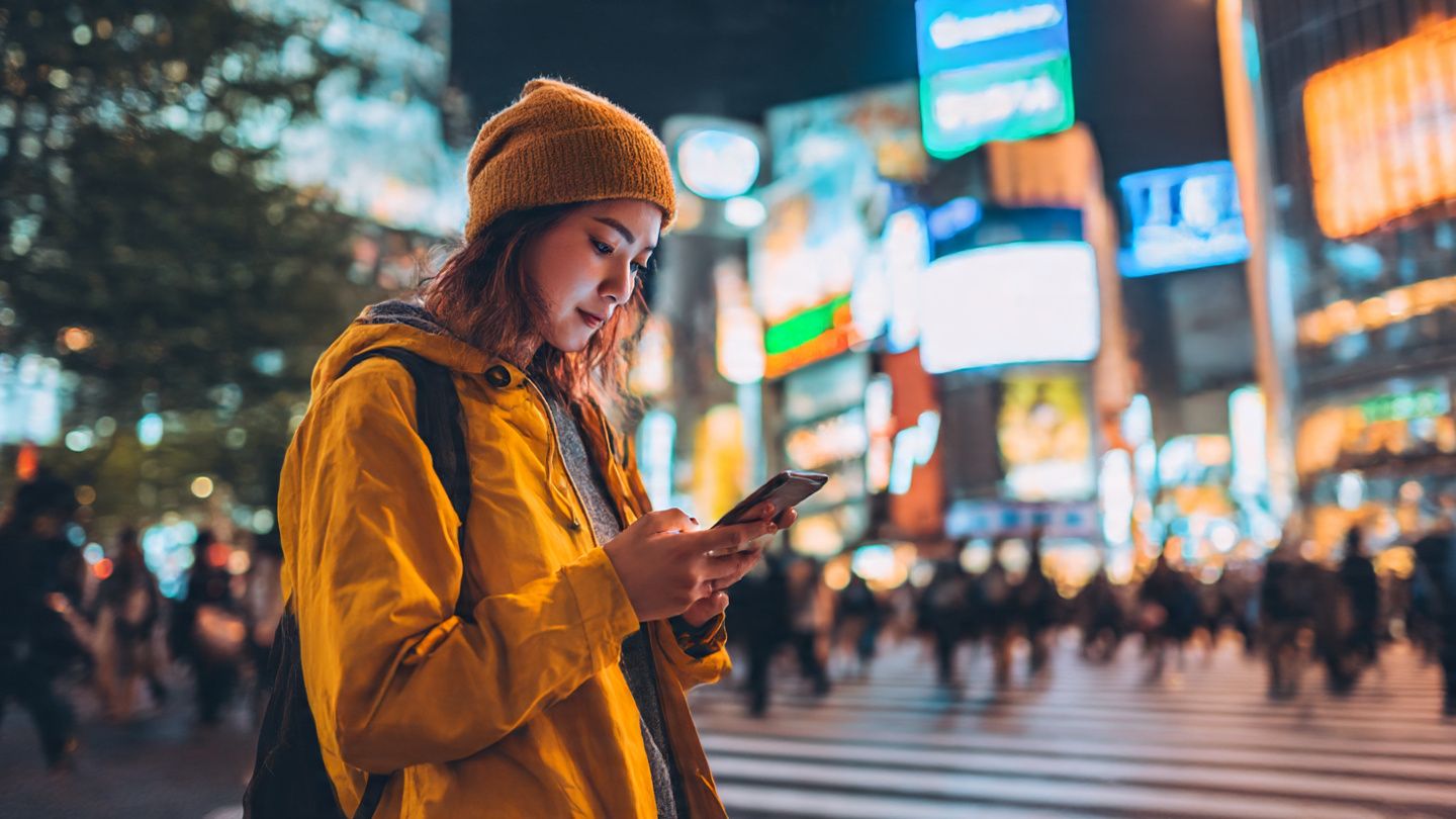 Traveler using a smartphone in Shibuya Crossing, Tokyo, enjoying fast eSIM internet access — bright city lights, modern vibe, connectivity theme.