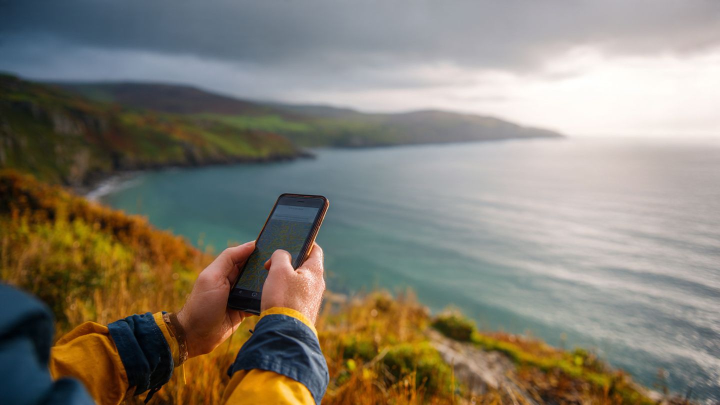 Image of traveler using a smartphone with UK mobile signal while scenic Northern Ireland coast fades in the background