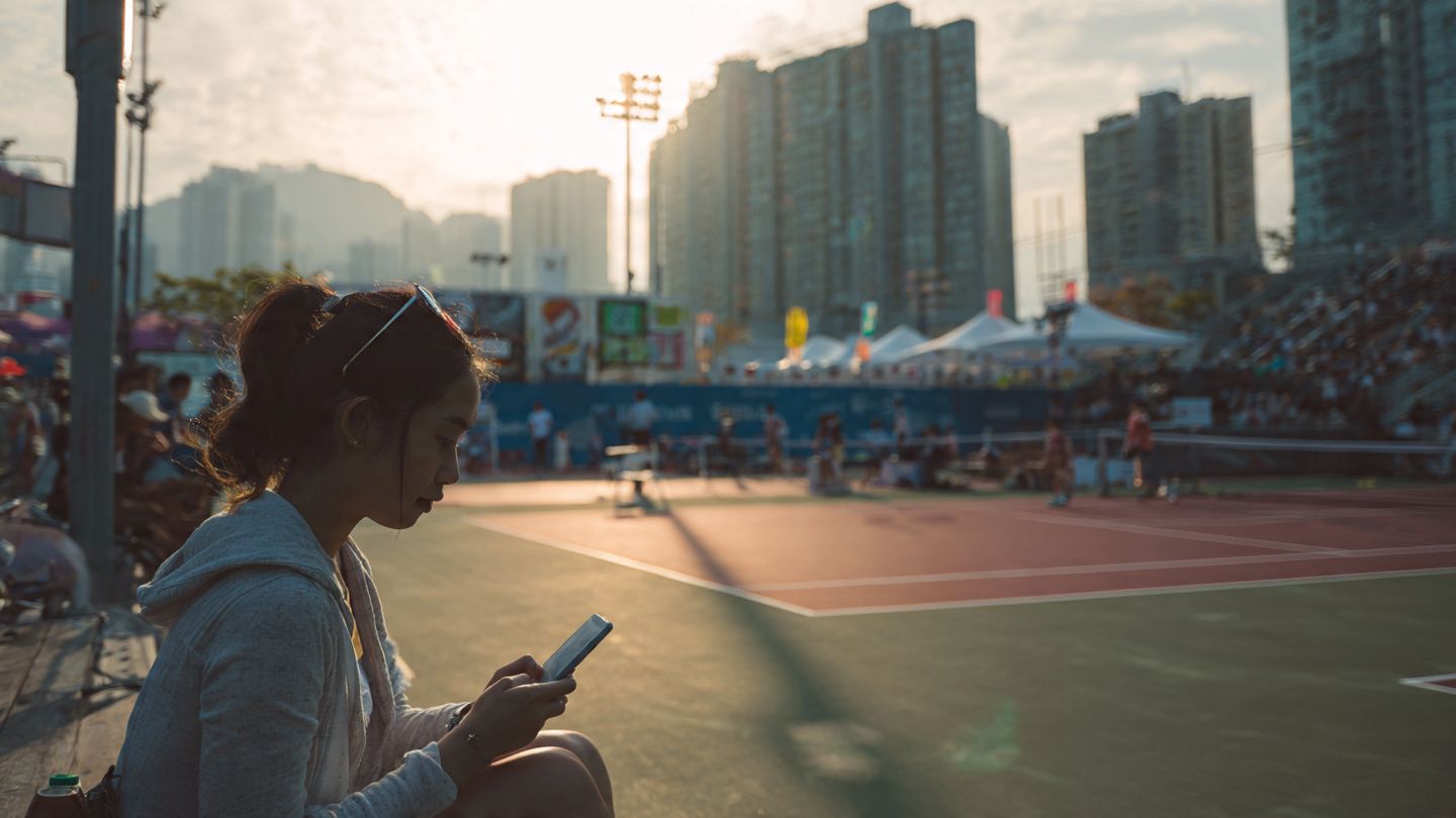 Traveler using smartphone near Hong Kong’s Victoria Park tennis stadium, warm daylight, modern editorial style — for demonstrating mobile connectivity setup