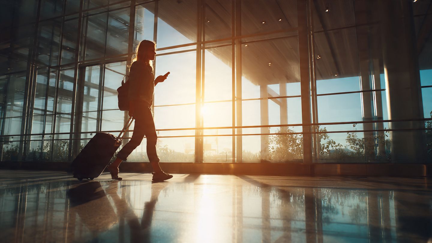 Traveler walking through Perth Airport arrivals with luggage, checking phone displaying active eSIM signal; bright natural light, modern travel aesthetic