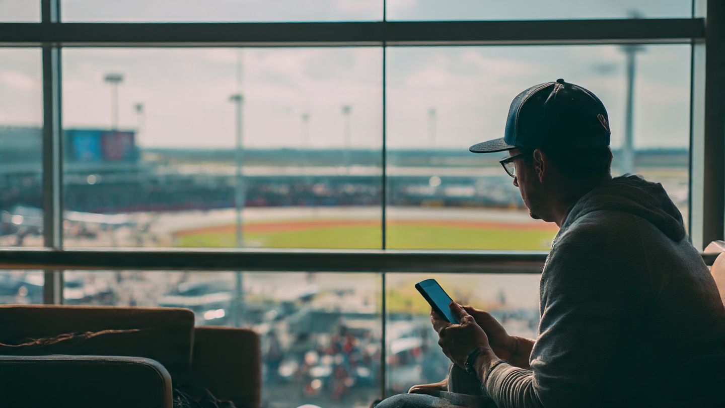 Traveler watching a live baseball game on a smartphone at an airport lounge, symbolizing easy connectivity and sports passion worldwide