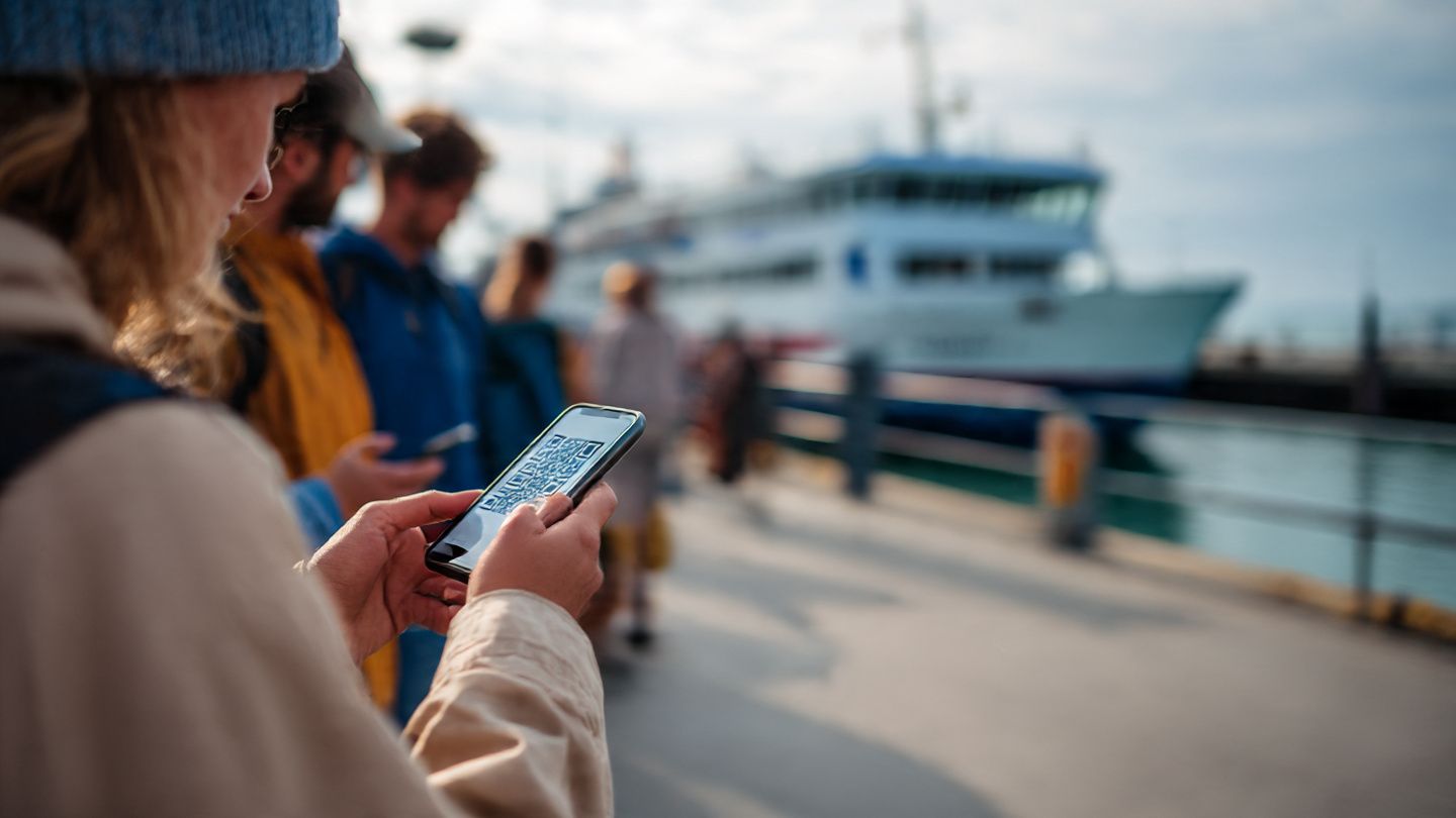Travelers scanning a QR code on a smartphone near a ferry terminal, symbolizing easy eSIM setup before boarding to Heligoland.